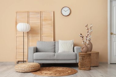 Gri kanepe, puf, hasır masalar ve oturma odasının içinde pamuk çiçekli vazolar.