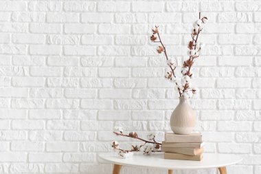 Oturma odasındaki masada pamuk çiçekli kitap ve vazo, yakın plan.