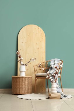 Hasır masa, koltuk ve vazolarla yeşil duvarın yanında, oturma odasının içinde pamuk çiçekler.