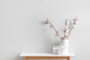 Oturma odasında, üzerinde pamuk çiçekleri ve ev şeklinde heykelcikler olan bir vazo.