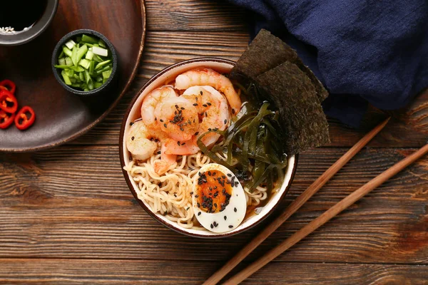 Bir kase erişte çorbası, karides ve ahşap zemin üzerinde yosun örtüleri.