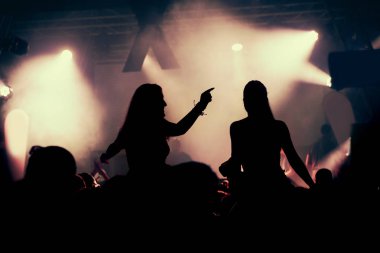Parlak sahne ışıkları önünde konser kalabalığının siluetleri