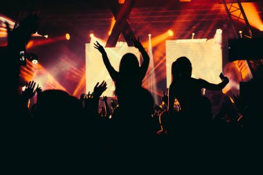 Parlak sahne ışıkları önünde konser kalabalığının siluetleri