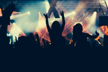 Parlak sahne ışıkları önünde konser kalabalığının siluetleri