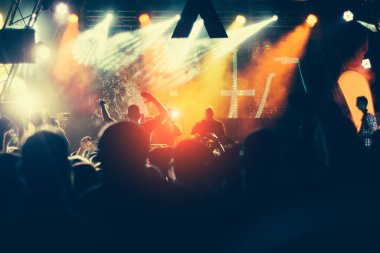 Parlak sahne ışıkları önünde konser kalabalığının siluetleri
