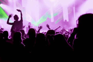 Parlak sahne ışıkları önünde konser kalabalığının siluetleri