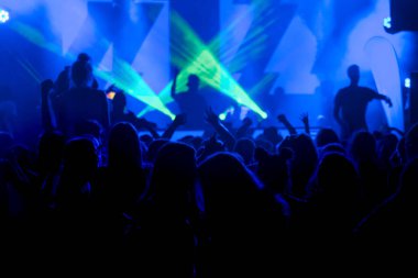 Parlak sahne ışıkları önünde konser kalabalığının siluetleri