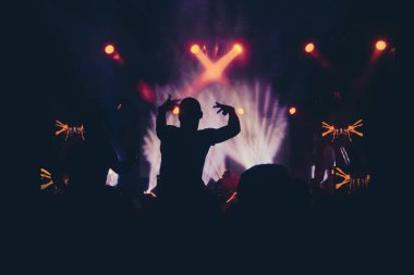 Parlak sahne ışıkları önünde konser kalabalığının siluetleri