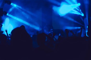 Parlak sahne ışıkları önünde konser kalabalığının siluetleri