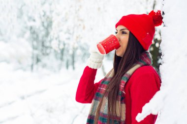 Genç kadın bir örgü şeklinde bir kar yağışı sırasında ormanda çay içme.