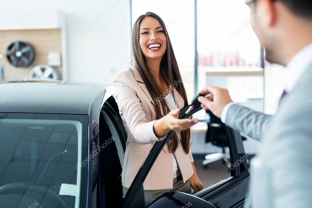 Happy woman holding keys to her new car at the dealership