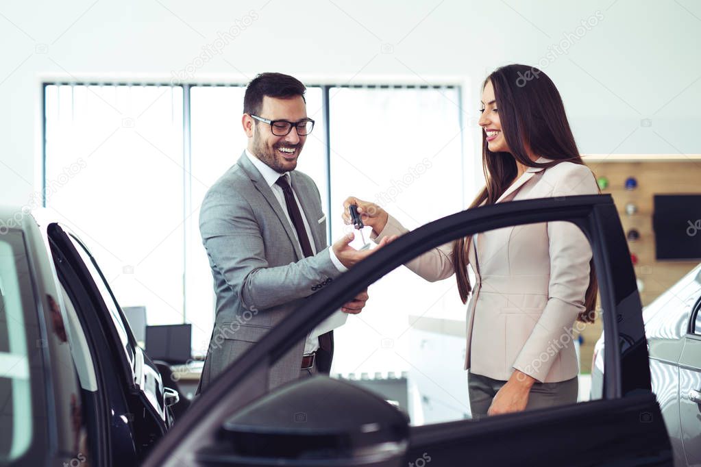 Saleswoman giving keys of new car to male client 
