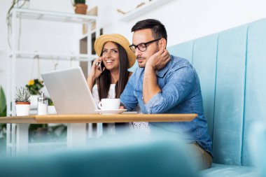 Kafede oturan bir çift neşeyle gülüyor, dizüstü bilgisayar ekranına bakıyor