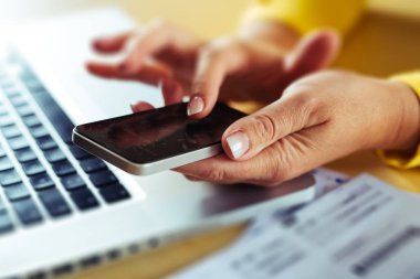 Bilgisayarda çalışırken akıllı telefon kullanan kadın eller. İş kadını cep telefonuna mesaj yazıyor..