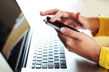 Bilgisayarda çalışırken akıllı telefon kullanan kadın eller. İş kadını cep telefonuna mesaj yazıyor..