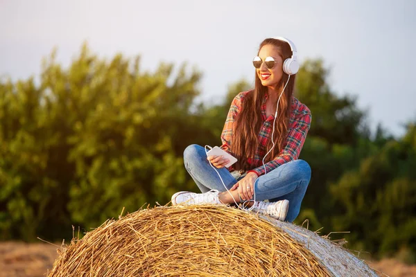 Kız kulaklık la buğday tarlasında oturuyor. Sırtını samanlıkta yaslanıyor..