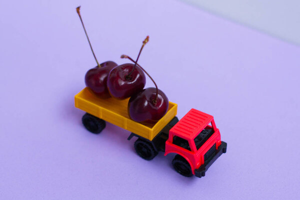 A toy car carries ripe cherries - delivery of berries and fruits.