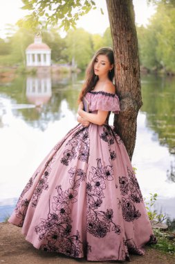 19. yüzyıl elbisesi içinde güzel bir genç kadın elinde bir kitapla parkta duruyor. Gölette romantik bir kız.