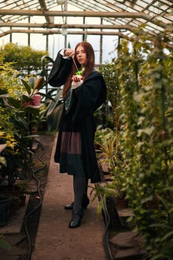 Elinde sihirli değnekle genç büyücüler okulundan bir kız. Yeşil büyü. Bir büyücü seradaki bitkiler arasında hokkabazlık yapar, botanik dersi ise kostümdür..