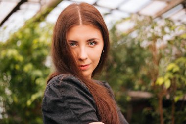 Bir seranın arka planında uzun saçlı bir kızın portresi, yakın plan.