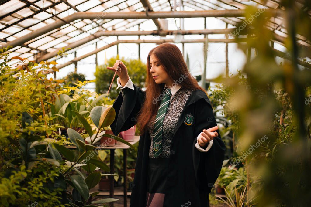 Kopeysk, Chelyabinsk / Russia - 10/02/2019: A girl from the school of young wizards with a magic wand in his hand. A sorceress conjures among plants in a greenhouse, a botany lesson.