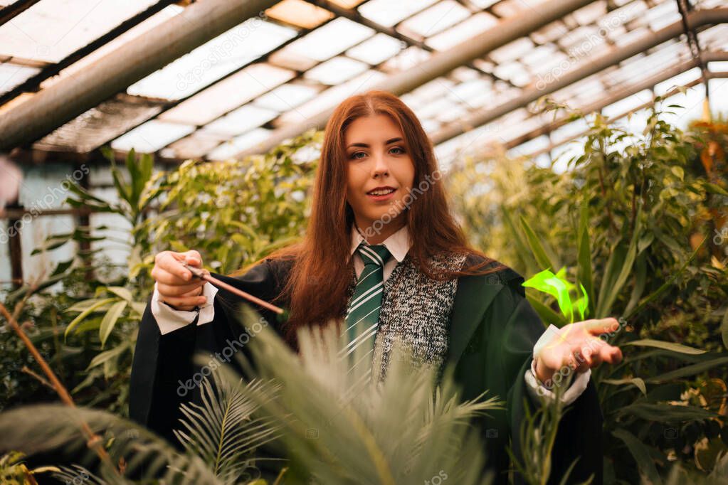 A girl from the school of young wizards with a magic wand in his hand. Green magic. A sorceress conjures among plants in a greenhouse, a botany lesson is cosplay.