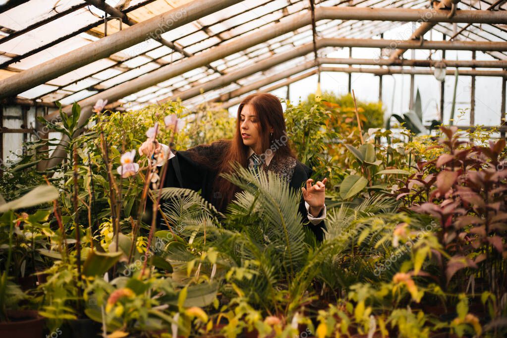 A girl from the school of young wizards with a magic wand in his hand. Green magic. A sorceress conjures among plants in a greenhouse, a botany lesson is cosplay.