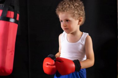 Kırmızı boks eldivenli küçük bir çocuk boks çantasına vurmak için antrenman yapıyor. Spor, çocuk boksu..