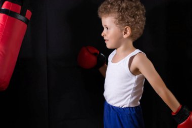 Kırmızı boks eldivenli küçük bir çocuk boks çantasına vurmak için antrenman yapıyor. Spor, çocuk boksu..
