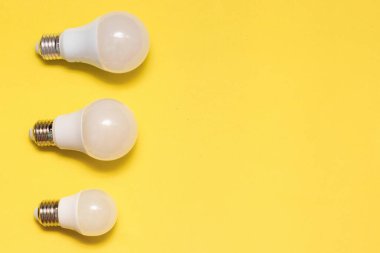 Sarı arka planda farklı boyutlarda üç LED lamba. Elektrik tasarrufu kavramı. Metin için yer, kopyalama alanı.
