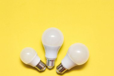 Sarı arka planda farklı boyutlarda üç LED lamba. Elektrik tasarrufu kavramı. Metin için yer, kopyalama alanı.
