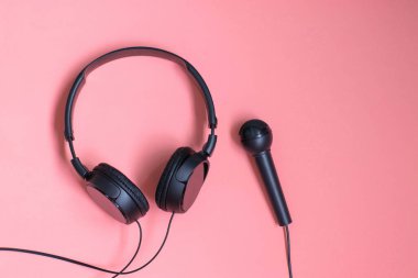 Pembe arka planda kulaklık ve mikrofon. Şarkı söyleme ve müzik dersleri kavramı.
