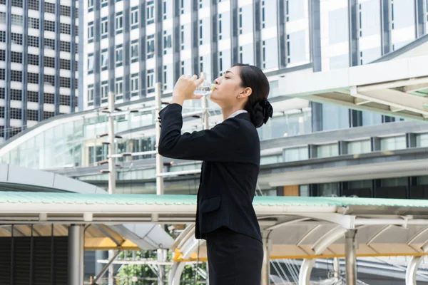 Asiatisk forretningskvinne som står og drikker rent mineralvann fra plastflaske på varm sommerdag – stockfoto