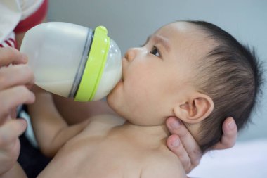 Küçük bebek beslenme şişesinden süt emer. Annesi tarafından taşınmış..