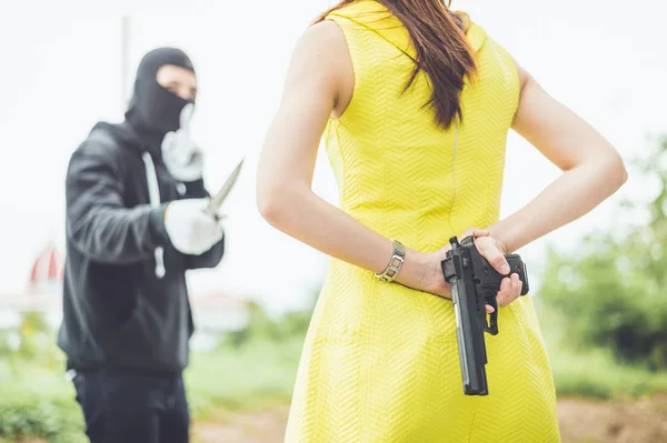 Преступник или бандит носить черную маску использовать нож указывают на женщину, пытающуюся ограбить деньги и причинить ей боль, но женщина, но женщины спрятали свое оружие behin, концепция победителя, борьба, узурпация Лицензионные Стоковые Фото