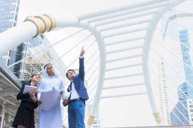 Arap işadamı projeyi elinde tutuyor ve Asyalı işadamı ve iş kadınıyla inşaat sürecinden bahsediyor. metin için kopyalama alanı ile