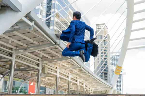 Movimento borrado de empresário asiático em uso formal segurando pasta enquanto corria e pular na cidade em um fundo de edifício. tarde para o conceito de trabalho Fotos De Bancos De Imagens