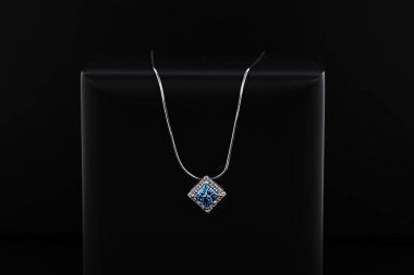 Siyah bir yüzeyde mavi ve beyaz bir kolye bulunur. Kolye gümüşten yapılmış ve elmas bir kolyesi var. Kolye basit ve zarif, modern bir tasarımı var.