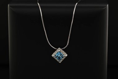 Siyah bir yüzeyde mavi ve beyaz bir kolye bulunur. Kolye gümüşten yapılmış ve elmas bir kolyesi var. Kolye basit ve zarif, modern bir tasarımı var.