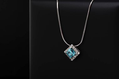 Siyah bir yüzeyde mavi ve beyaz bir kolye bulunur. Kolye gümüşten yapılmış ve elmas bir kolyesi var. Kolye basit ve zarif, modern bir tasarımı var.