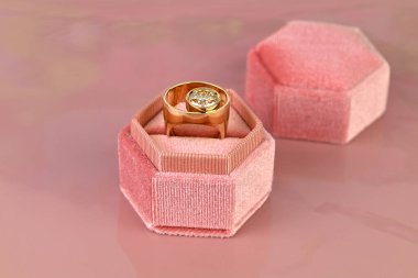 Pembe kadife bir kutuda bir yüzük var. Yüzük sarı ve ortasında bir elmas var.