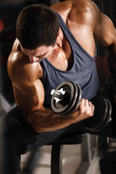 Fitness in sportschool, sport en een gezonde levensstijl concept. Knappe atletische man in blauw shirt die oefeningen maakt. Bodybuilder mannelijk model training biceps spieren met halter — Stockfoto