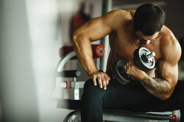 Fitness tornaterem, sport és egészséges életmód koncepció. Jóképű sportoló, meztelen felsőtesttel, gyakorlatokat csinál. Testépítő férfi modell képzés bicepsz izmok súlyzóval — Stock Fotó