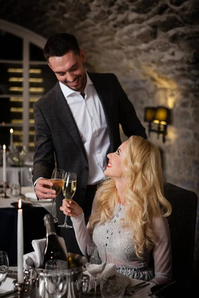 Romantyczne i randkowe pojęcie. Młoda para mężczyzna i kobieta w kieliszkach do szampana świętują i wznoszą toast w restauracji. Dwie osoby mężczyzna i kobieta w eleganckim stroju wieczorowym i sukienka na romantyczną kolację — Zdjęcie stockowe