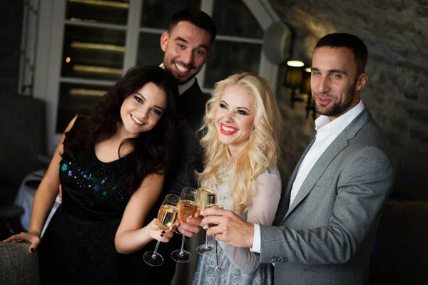 Fête, vacances avec des amis concept. Quatre personnes avec des verres de champagne célébrant et grillant au restaurant. Deux hommes et deux femmes dans des vêtements de soirée élégants, costumes et robes de nuit à l'intérieur — Photo