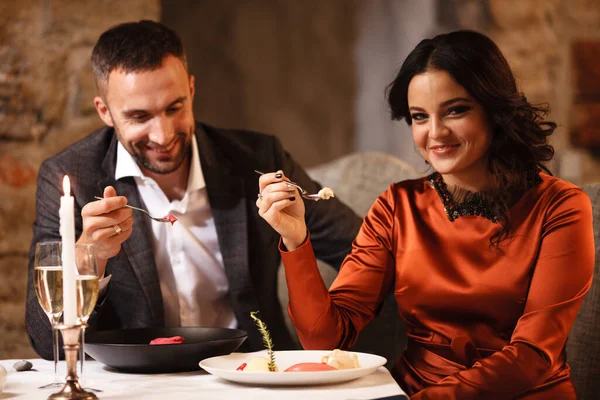 Romance e namoro conceito. Jovem casal homem e mulher comemorando e comendo deliciosa sobremesa no restaurante. Duas pessoas macho e fêmea em elegante terno de noite e vestido em jantar romântico — Fotografia de Stock