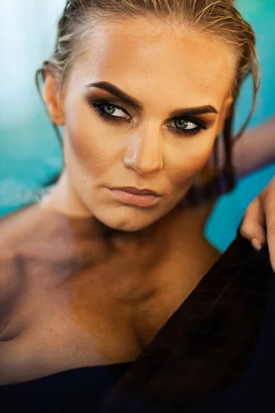 Ontspanning en spa concept. Portret van een sexy modieuze dame in een zwart badpak. Vrouw met nat haar en make-up poseert in water in het zwembad in natuurlijk zonlicht — Stockfoto