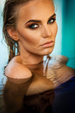 Rahatlama ve spa konsepti. Siyah mayo giymiş seksi, şık bir kadının portresi. Islak saçlı ve makyajlı bir kadın, güneş ışığında yüzme havuzunda poz verir.