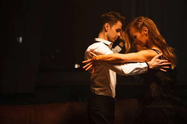 Concept de danse et d'amour. Jeune couple dans des robes de soirée élégantes posant dans la chambre remplie de lumière dramatique. Deux danseurs homme et femme se tenant l'un l'autre dans une pose passionnée — Photo