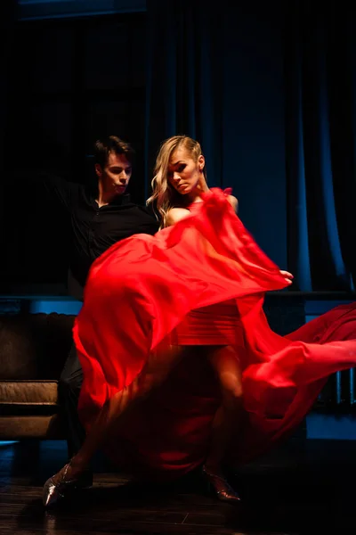 Koncept tance a lásky. Mladý pár v elegantních večerních šatech pózuje v místnosti naplněné dramatickým světlem. Dva tanečníci muž a žena drží jeden druhého v vášnivé póze — Stock fotografie